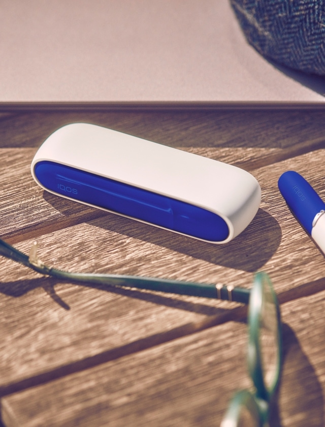 An IQOS device and holder on a wooden surface.